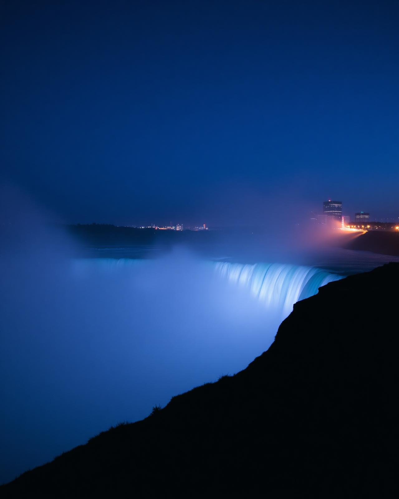 Niagara Falls illuminated at blue hour with distant city lights